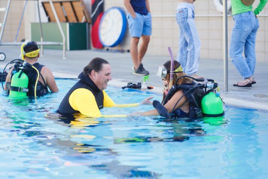 Doug Hayes helping a student put on SCUBA gear at the BRIC pool 