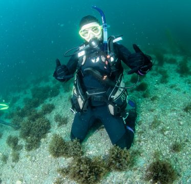 A student SCUBA diving in the ocean holding up “Shaka” symbol with hands 