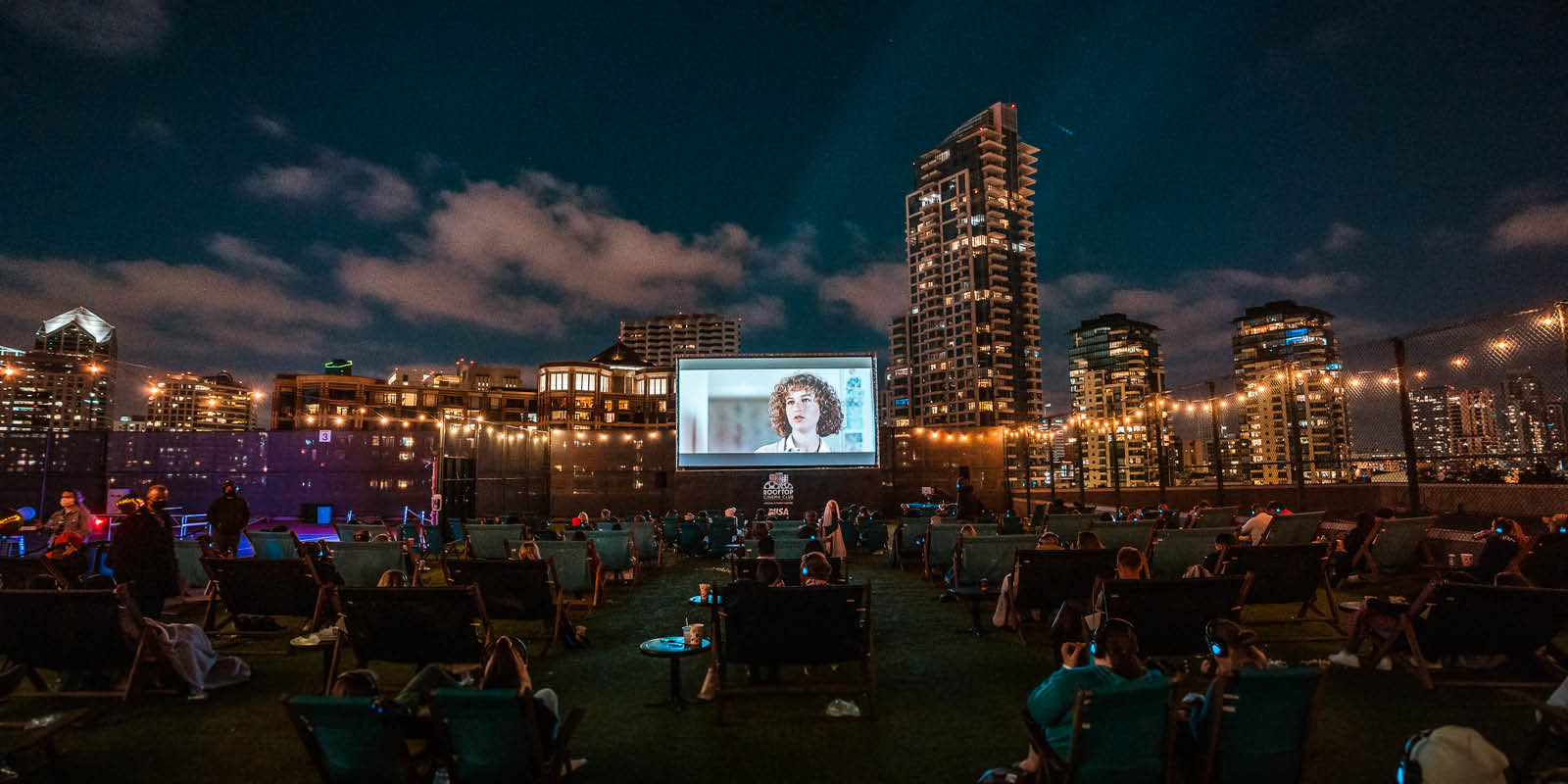 people sitting on lawn chairs at night watching a movie on screen