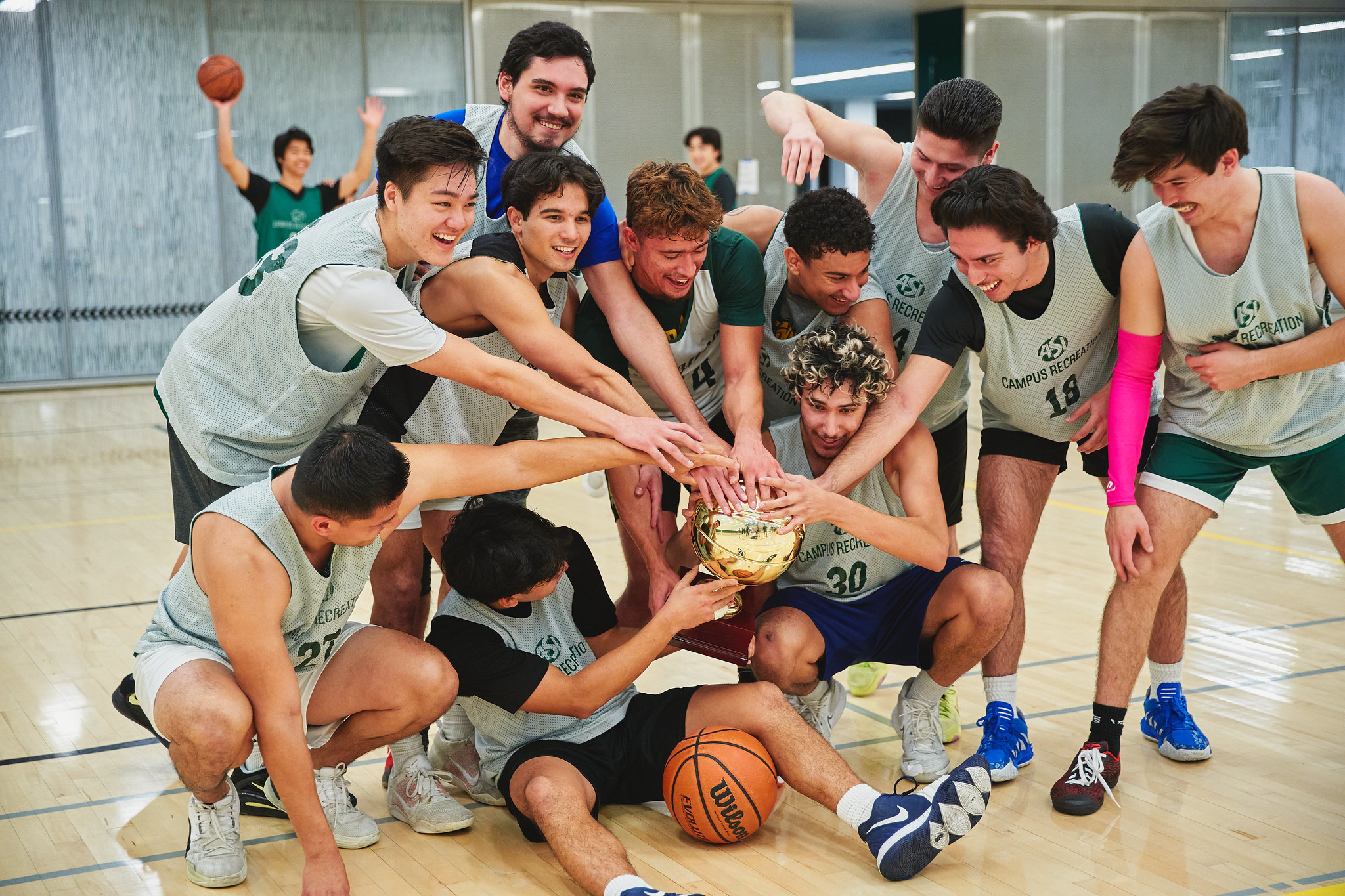 Group of basketball players in grey basketball jerseys holding a trophy.