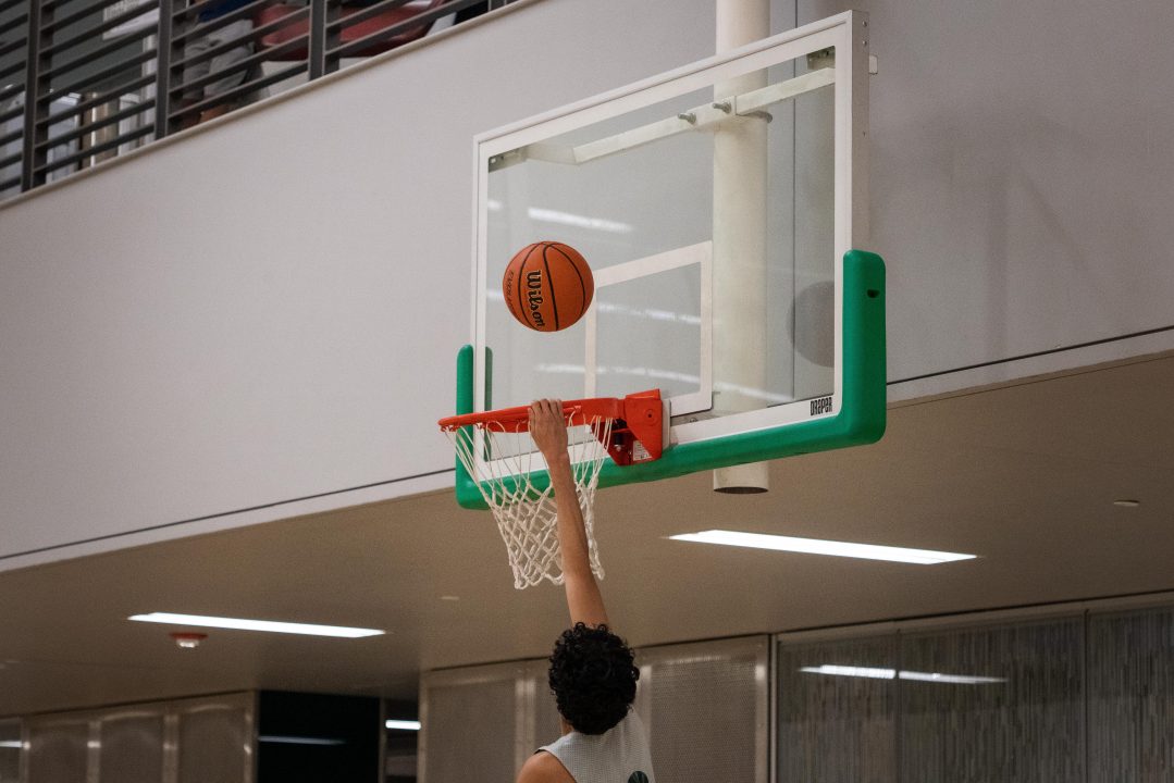 Student hanging on to basketball hoop.