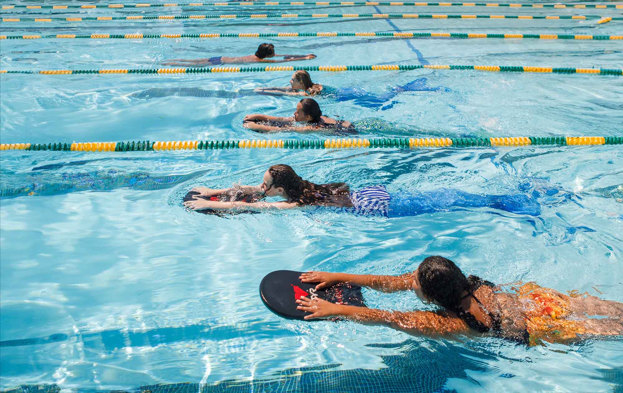 students using kick boards to swim lanes in a pool