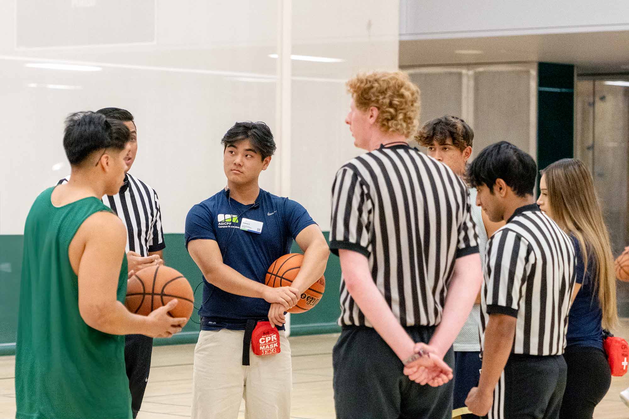 student staff and referees talking to basketball players in a huddle