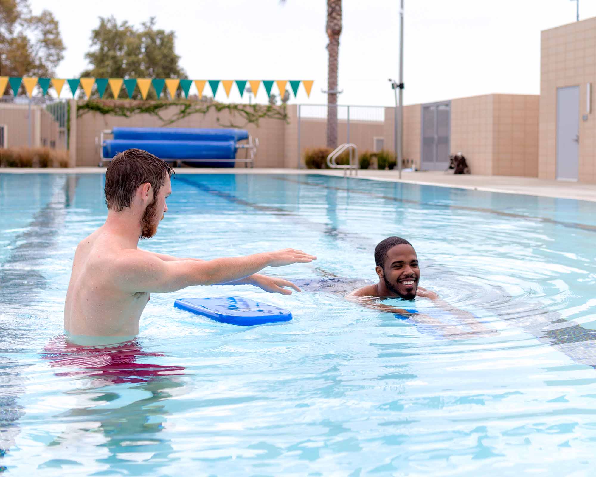 Swim instructor teaching a participant how to swim with a kick board