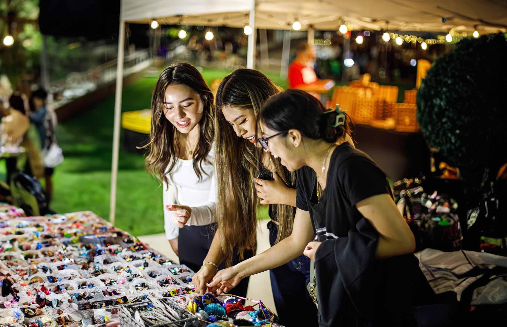 Three people looking at merchandise on a table at an outdoor night market