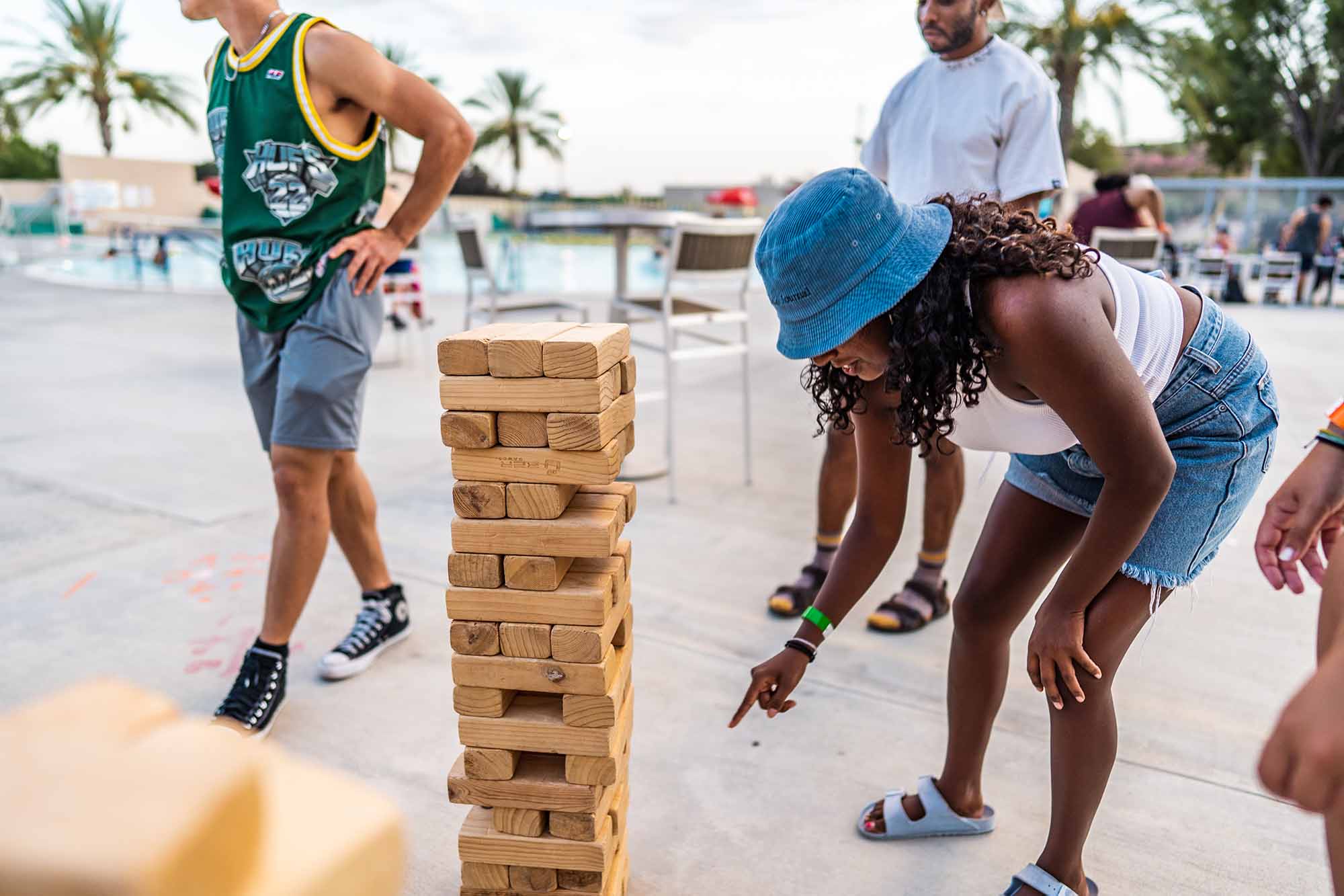 People playing a large-scale Jenga game by a pool